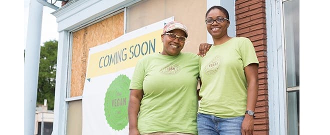 Two women business owners posing for a picture together next to their business sign