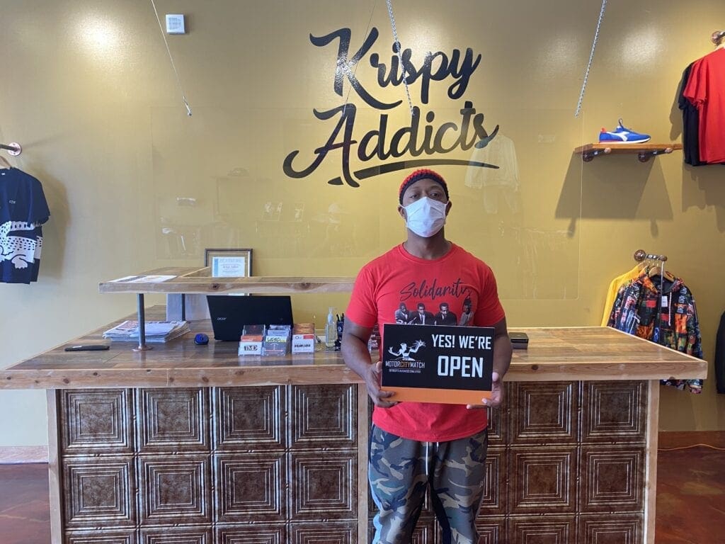 Charles Micheaux, co-owner of Krispy Addicts, poses with a sign indicating the clothing store is open for business